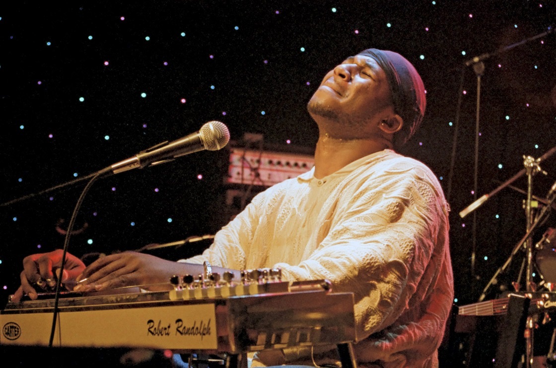 Robert Randolph tips his head back with eyes closed while playing pedal steel against a starry stage backdrop.